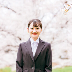 桜の花を背にスーツを着て立つイメージ