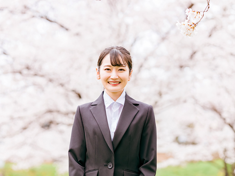 桜の花を背にスーツを着て立つイメージ