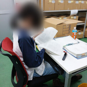 資料のスキャン準備として、ページ間に異物が挟まっていないか、紙の折れがないかを一枚ずつ丁寧に指差し確認する訓練生。細かな配慮がミスのない業務に繋がる。