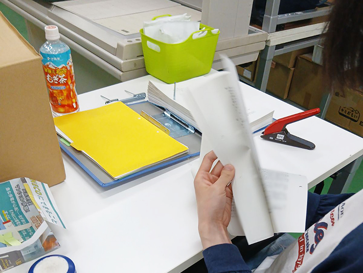 スキャン機に通す直前に、資料の間に何か挟まっていないか、また紙に折れなどがないかを細かく確認している真剣な表情。