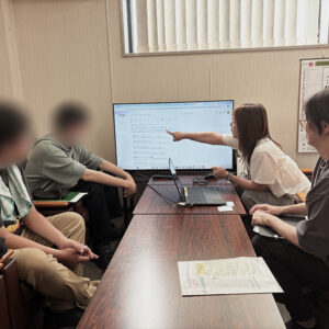障碍者ITカレッジ愛西の就労支援員・安井よしえが、Google検索結果に表示されたハローワークインターネットサービスの公式サイトを指差し、正しいページへのアクセス方法を訓練生にレクチャーしている様子。
