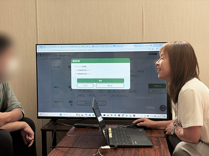 「正社員」や「パート」などの雇用形態を選択するチェックボックスが並ぶ画面を前に、就労支援員の安井が訓練生の「理想の働き方」についてじっくりと耳を傾け、一緒に求人を探す伴走支援の風景。