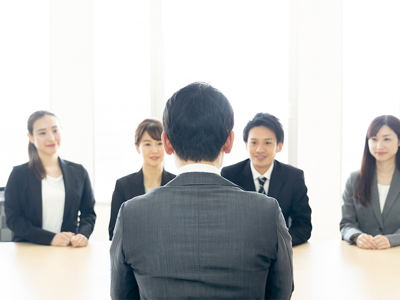 企業の面接官数名と向き合い、自身の強みや訓練での積み重ねを丁寧に伝える就活生のイメージ。沈黙を恐れず「少しお時間をいただけますか」と正直に伝えるテクニックを活かし、信頼関係を築こうとする模擬面接のような風景。