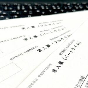 パソコンのキーボードの手前に「求人票（フルタイム）」「求人票（パートタイム）」と書かれたハローワーク等の実際の求人票用紙が何枚か重なって置かれている写真。就職活動を始める際にまず目にする求人票の全体像や、雇用形態による違いを意識して確認するカリキュラムの始まりを象徴するイメージ画像。