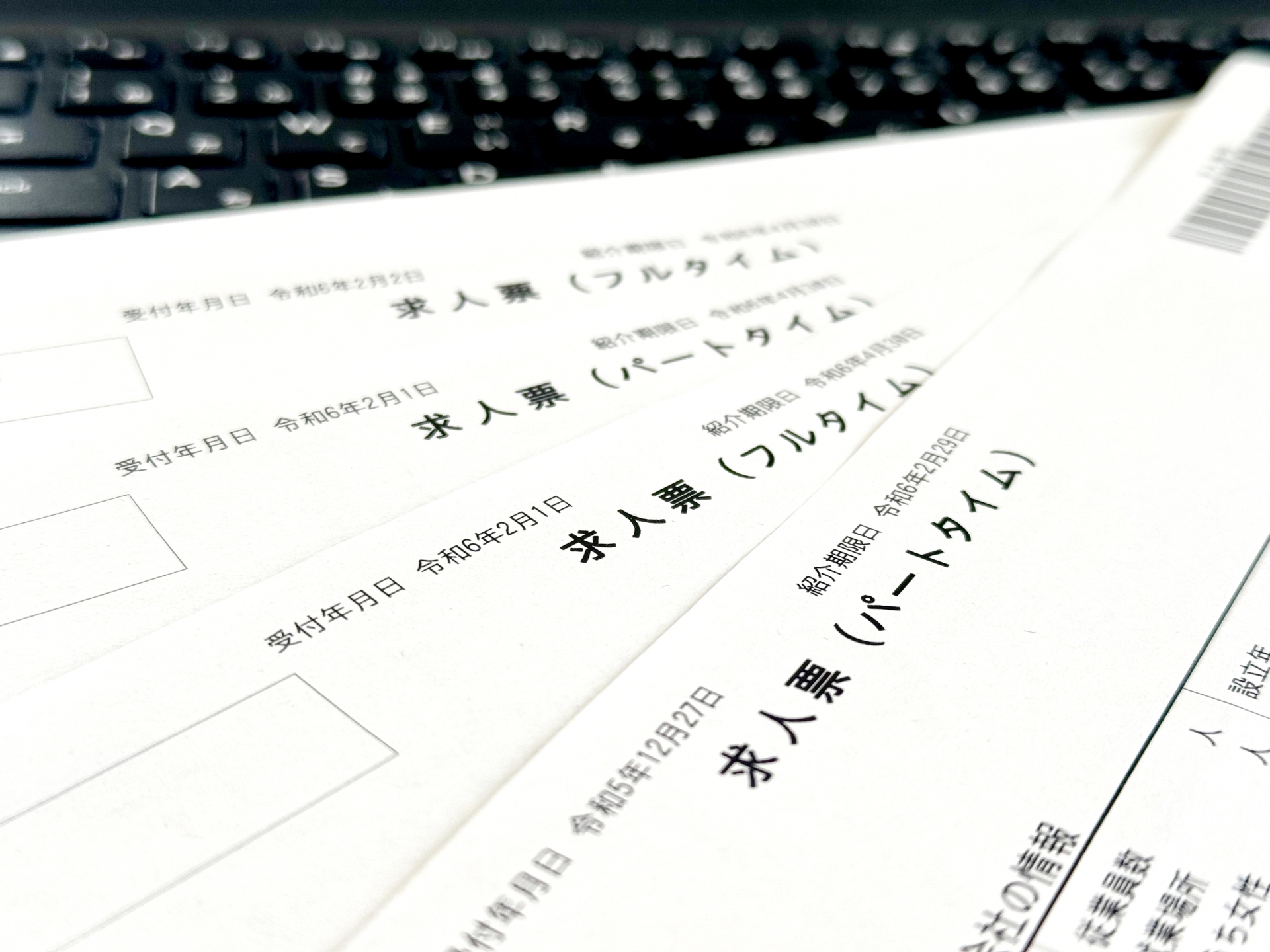 パソコンのキーボードの手前に「求人票（フルタイム）」「求人票（パートタイム）」と書かれたハローワーク等の実際の求人票用紙が何枚か重なって置かれている写真。就職活動を始める際にまず目にする求人票の全体像や、雇用形態による違いを意識して確認するカリキュラムの始まりを象徴するイメージ画像。